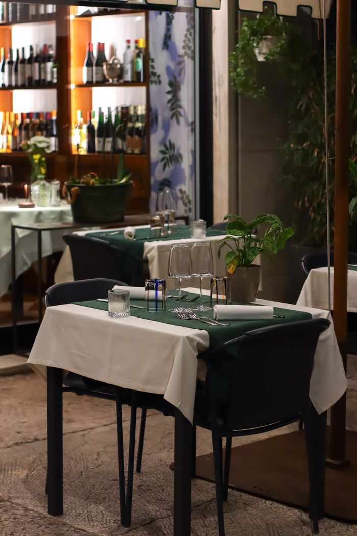 Elegant outdoor dining setup at a restaurant, featuring neatly arranged tables with glasses and plants.